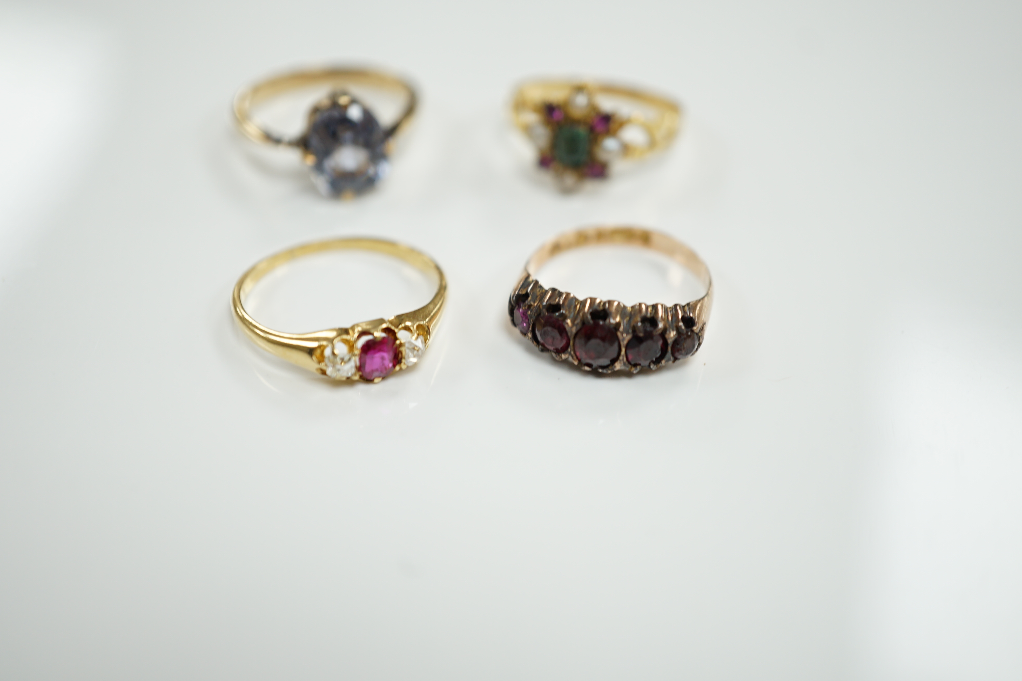 A late Victorian yellow metal, emerald, garnet and split pearl cluster set ring, in the Suffragette colours, size M/N and three other rings including Victorian 9ct gold and garnet set half hoop and 18ct, ruby and diamond